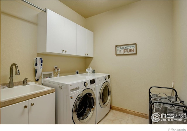 clothes washing area featuring washing machine and dryer, light tile patterned floors, baseboards, a sink, and cabinet space