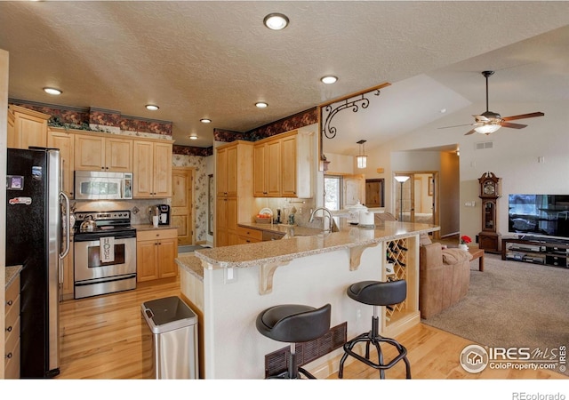 kitchen with a peninsula, a breakfast bar area, stainless steel appliances, open floor plan, and ceiling fan