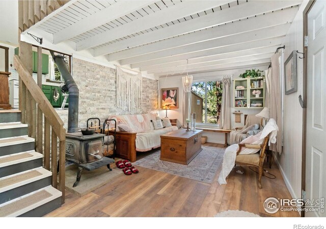 interior space featuring a wood stove, beam ceiling, wood finished floors, and stairs