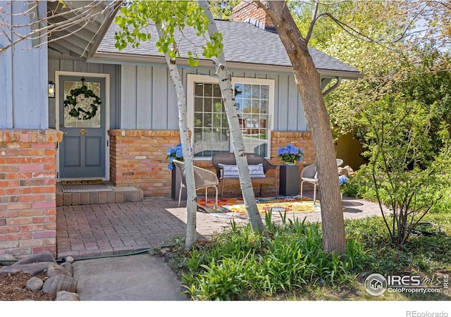 property entrance featuring board and batten siding, brick siding, roof with shingles, and a patio area