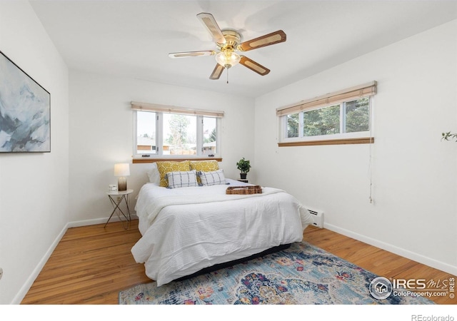 bedroom with baseboard heating, wood finished floors, baseboards, and ceiling fan