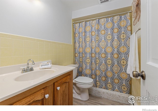 bathroom featuring tile walls, toilet, curtained shower, vanity, and a wainscoted wall