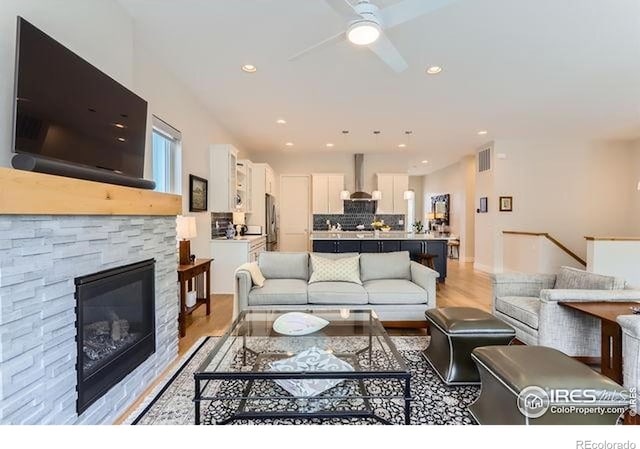living room with ceiling fan, light wood-style flooring, a stone fireplace, and visible vents