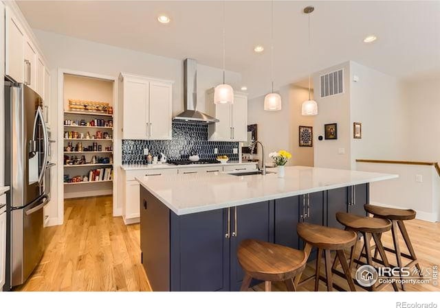 kitchen featuring visible vents, a sink, stainless steel fridge, wall chimney range hood, and light wood-style floors