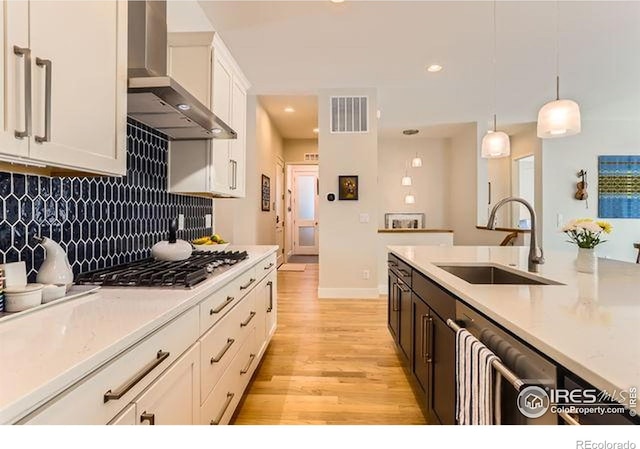 kitchen with a sink, stainless steel appliances, visible vents, wall chimney exhaust hood, and light wood-style floors