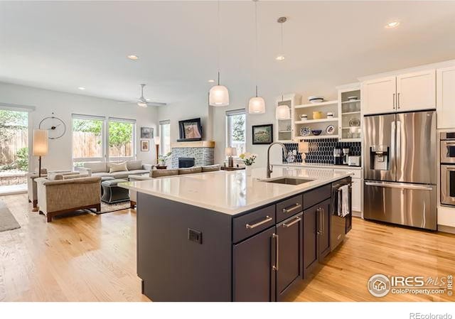 kitchen with a sink, stainless steel appliances, a fireplace, light countertops, and white cabinets
