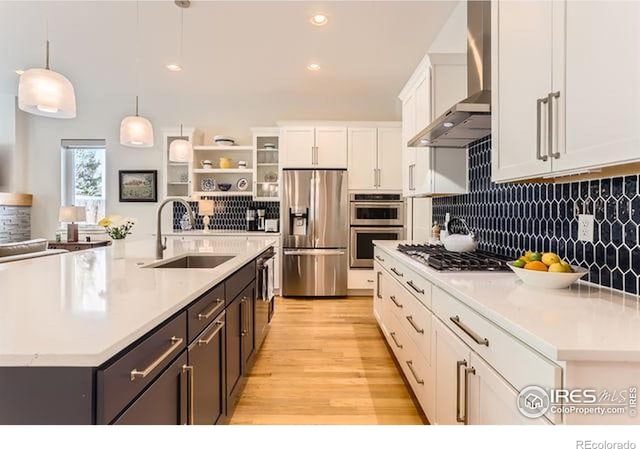 kitchen featuring stainless steel appliances, a sink, white cabinetry, wall chimney exhaust hood, and light countertops