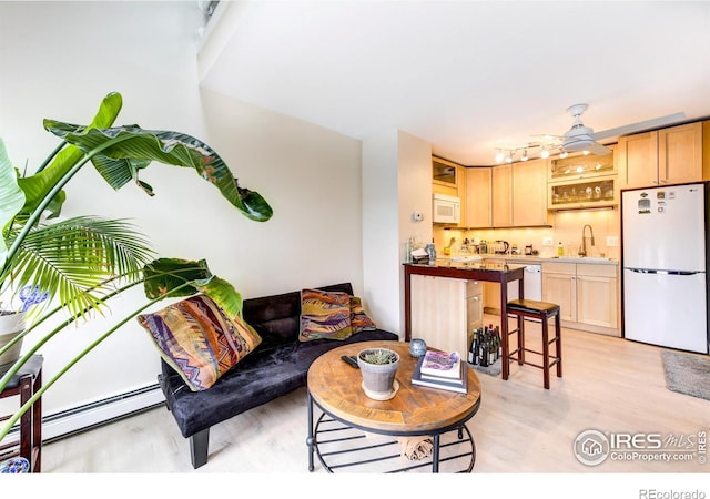 living room with a baseboard heating unit, light wood-style floors, and ceiling fan