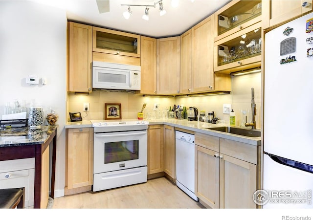kitchen with glass insert cabinets, white appliances, light wood finished floors, a sink, and tasteful backsplash