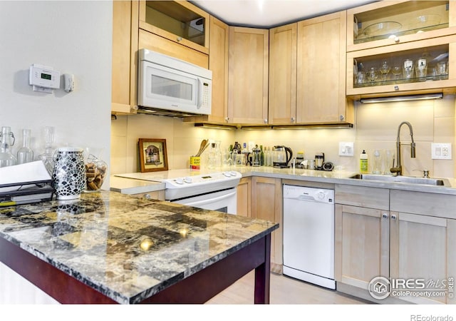 kitchen featuring light brown cabinets, glass insert cabinets, white appliances, a sink, and a peninsula