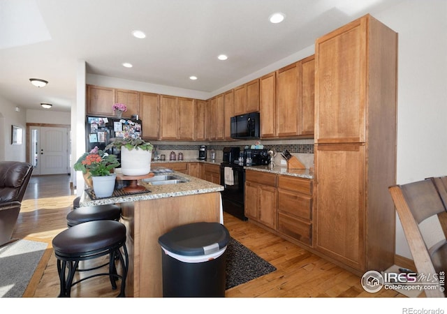 7084 Sumner St, Wellington, CO 80549 - kitchen with a kitchen breakfast bar, black appliances, recessed lighting, light wood finished floors, and decorative backsplash