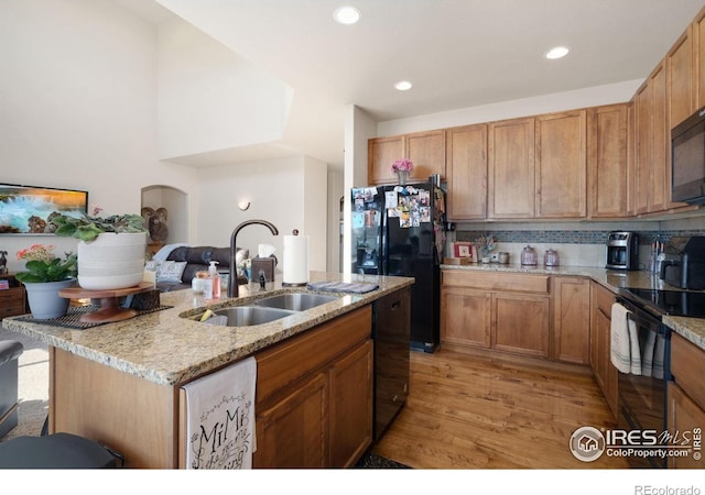 7084 Sumner St, Wellington, CO 80549 - kitchen featuring light stone counters, light wood finished floors, a sink, black appliances, and a kitchen island with sink