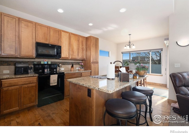 7084 Sumner St, Wellington, CO 80549 - kitchen featuring a notable chandelier, dark wood-style flooring, a kitchen bar, decorative backsplash, and black appliances