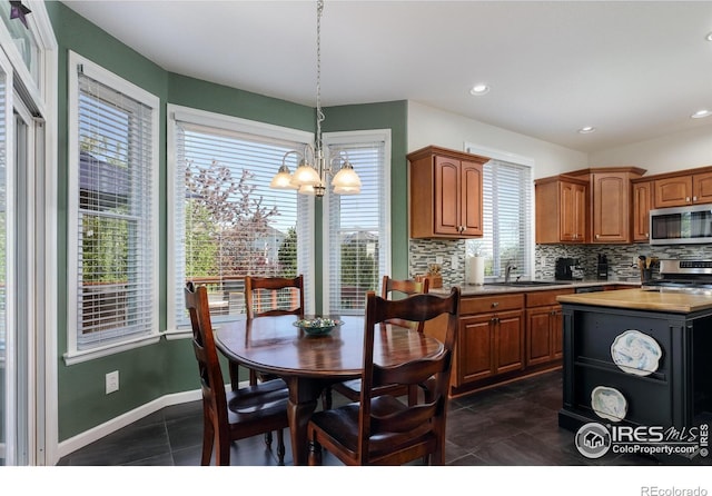 1809 Keel Ct, Lafayette, CO 80026 - kitchen with brown cabinets, an inviting chandelier, decorative backsplash, dark tile patterned flooring, and appliances with stainless steel finishes