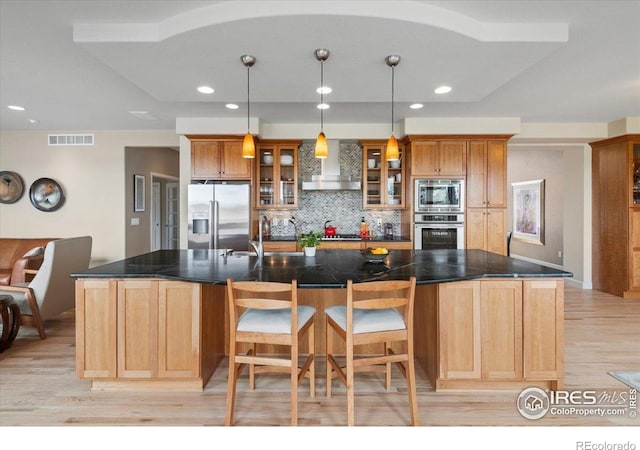 kitchen with tasteful backsplash, light wood-type flooring, visible vents, wall chimney exhaust hood, and appliances with stainless steel finishes
