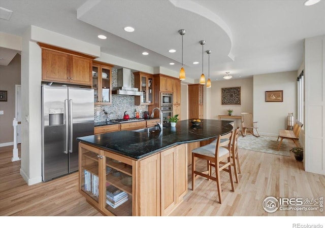 kitchen featuring stainless steel appliances, baseboards, wall chimney range hood, and light wood-style flooring