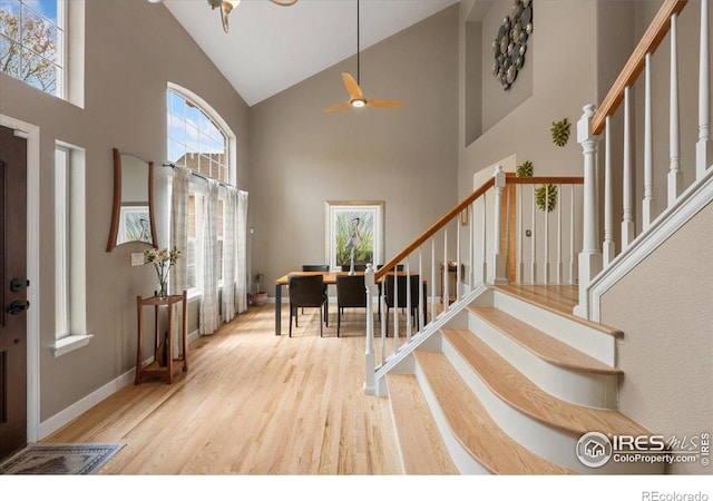 foyer with stairway, baseboards, high vaulted ceiling, and wood finished floors