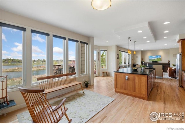 kitchen featuring light wood finished floors, freestanding refrigerator, dark countertops, brown cabinetry, and a kitchen island with sink