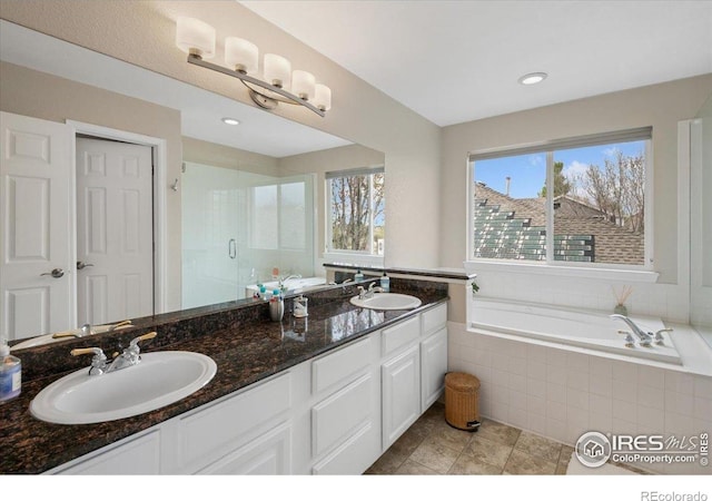 full bathroom featuring double vanity, a garden tub, a stall shower, and a sink