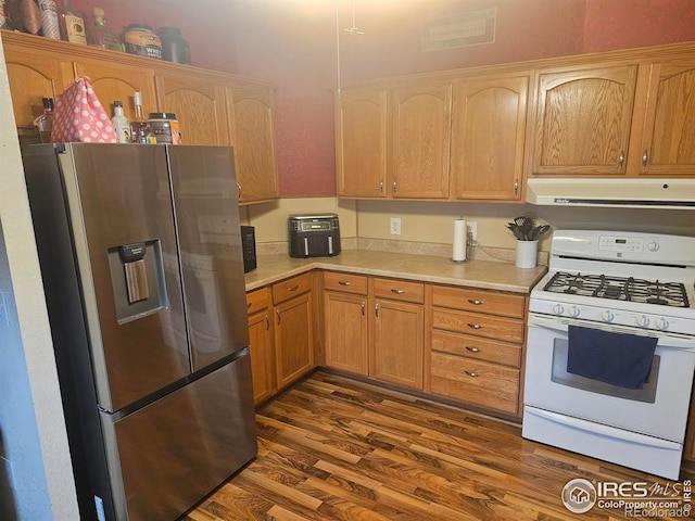 kitchen featuring gas range gas stove, ventilation hood, light countertops, stainless steel fridge, and dark wood-style floors