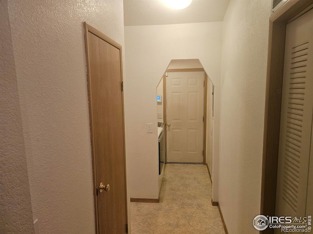 corridor with light colored carpet, baseboards, and a textured wall