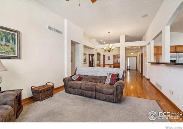 living room with ceiling fan with notable chandelier, visible vents, a high ceiling, and wood finished floors
