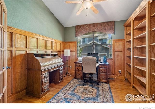home office with lofted ceiling, a decorative wall, a wainscoted wall, a ceiling fan, and light wood-style floors