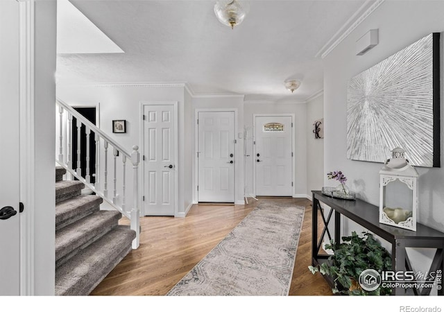 foyer with crown molding, wood finished floors, baseboards, and stairs
