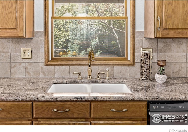 kitchen with a sink, brown cabinetry, tasteful backsplash, dishwashing machine, and light stone countertops