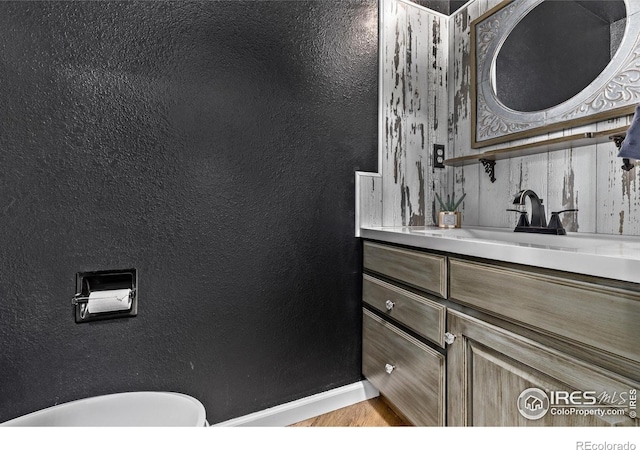 half bath with vanity, baseboards, and wood finished floors