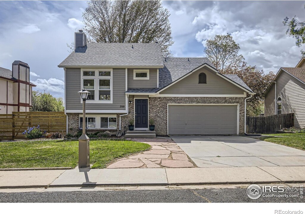 709 Buchanan Ln, Longmont, CO 80504 - view of front facade with an attached garage, concrete driveway, a chimney, and brick siding
