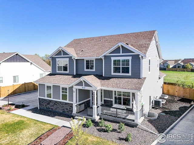 craftsman-style house with roof with shingles, covered porch, a fenced backyard, and stone siding