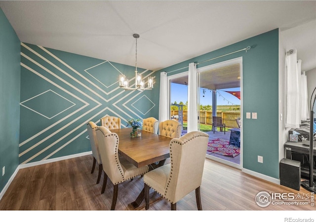 dining area with a chandelier, wood finished floors, baseboards, and an accent wall