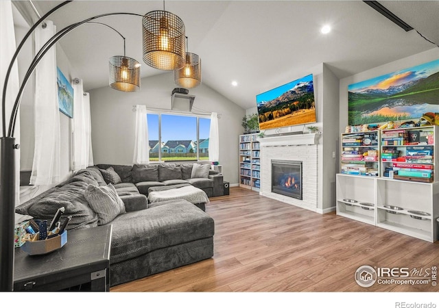 living area with lofted ceiling, wood finished floors, a glass covered fireplace, and recessed lighting