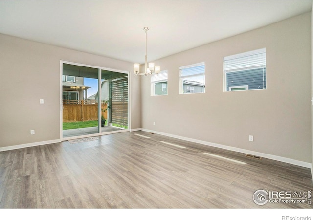 spare room with an inviting chandelier, wood finished floors, visible vents, and baseboards