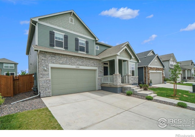 craftsman-style home featuring stone siding, covered porch, driveway, and fence