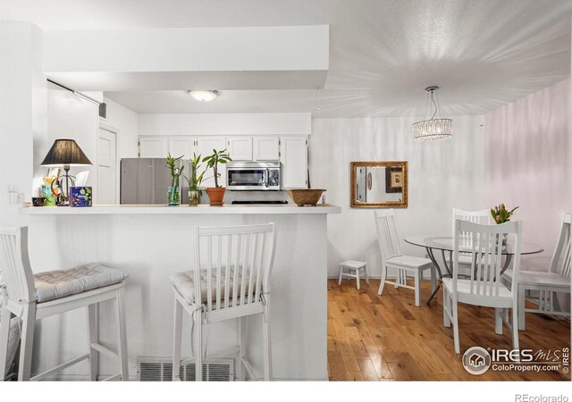 5086 Buckingham Rd, Boulder, CO 80301 - kitchen featuring stainless steel appliances, white cabinetry, a kitchen breakfast bar, light wood-type flooring, and a peninsula