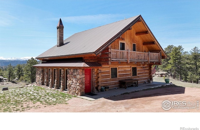 view of front of home featuring metal roof, a chimney, a balcony, and stone siding