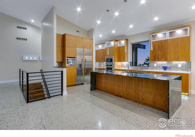 9360 Gold Mine Rd, Loveland, CO 80538 - kitchen featuring built in appliances, dark speckled floor, brown cabinets, tasteful backsplash, and a center island with sink