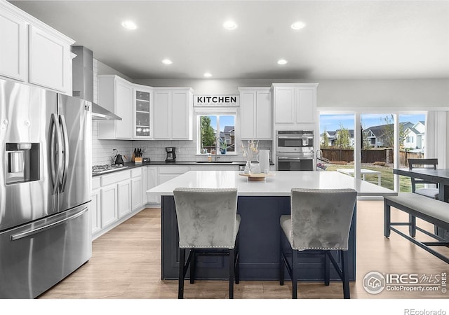 kitchen featuring stainless steel appliances, wall chimney exhaust hood, backsplash, a kitchen breakfast bar, and recessed lighting