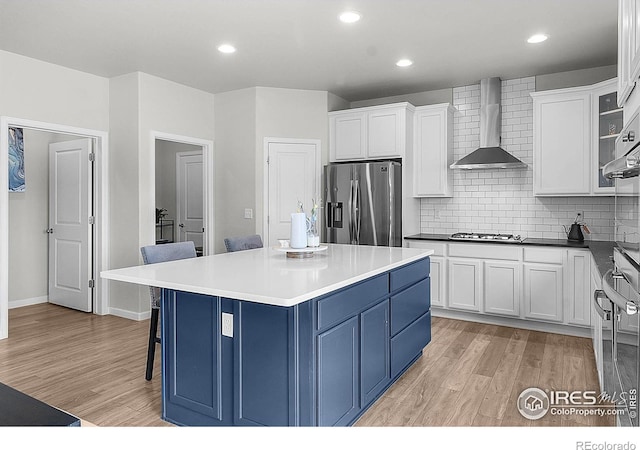 kitchen with stainless steel fridge with ice dispenser, wall chimney exhaust hood, blue cabinetry, light wood finished floors, and recessed lighting