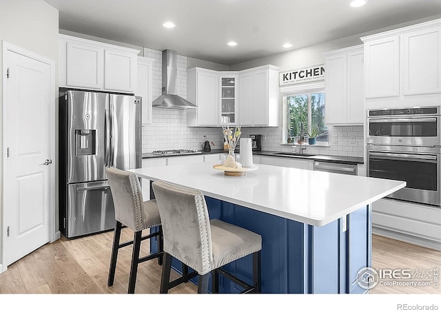kitchen featuring wall chimney range hood, appliances with stainless steel finishes, a sink, a kitchen breakfast bar, and a kitchen island