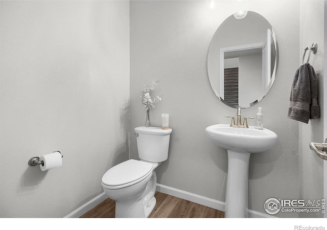 half bath featuring wood finished floors, toilet, and baseboards