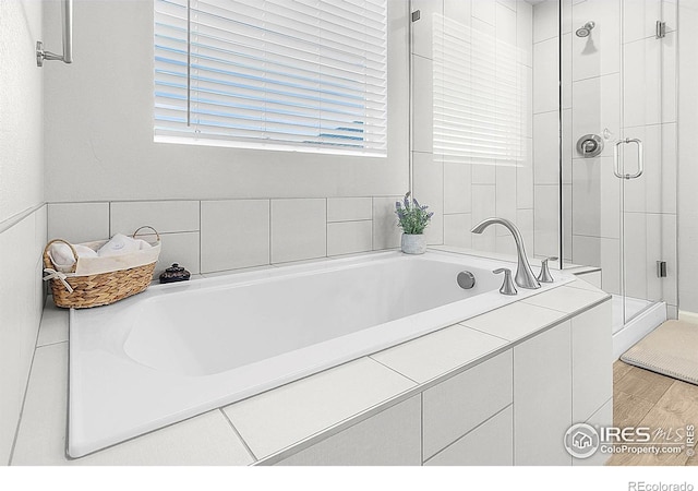 bathroom featuring a shower stall, plenty of natural light, wood finished floors, and a bath
