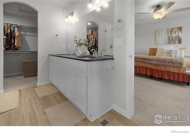 bathroom with ensuite bathroom, wood finished floors, double vanity, ceiling fan, and baseboards
