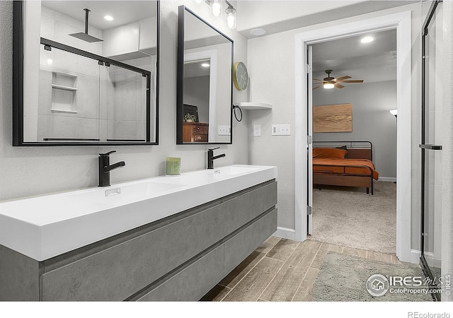 ensuite bathroom with wood finish floors, ceiling fan, a stall shower, double vanity, and baseboards
