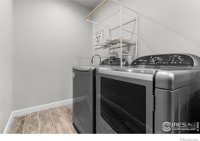 clothes washing area featuring washing machine and dryer, wood finished floors, and baseboards
