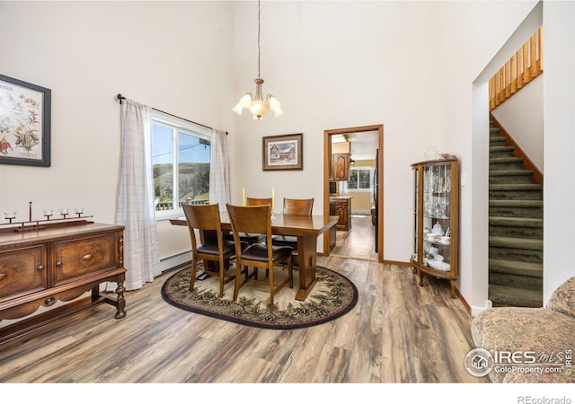 dining room with wood finished floors, a chandelier, baseboard heating, stairway, and a towering ceiling