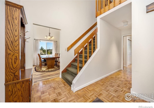 stairway featuring baseboards, a towering ceiling, and a chandelier