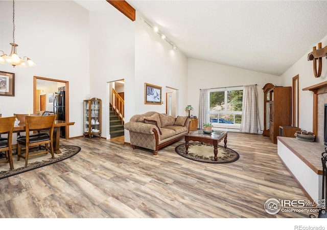 living room featuring stairway, a chandelier, high vaulted ceiling, wood finished floors, and rail lighting